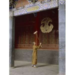 Robed Monk Strikes a Metal Gong with a Mallet at a Temple in China 